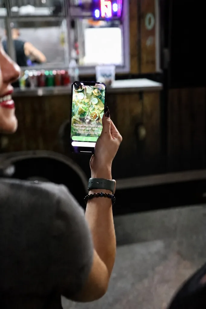 Customer holding a phone with Food T.R.X. at a food truck at night